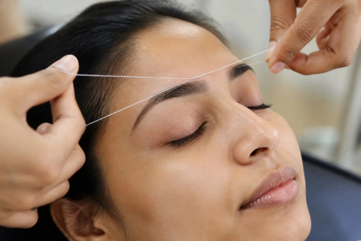 Close-up of eyebrow threading with twisted cotton thread shaping the brow line.